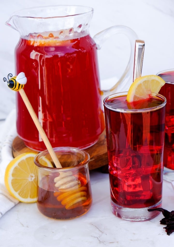 A pitcher of hibiscus lemonade with some honey to sweeten the drink. 