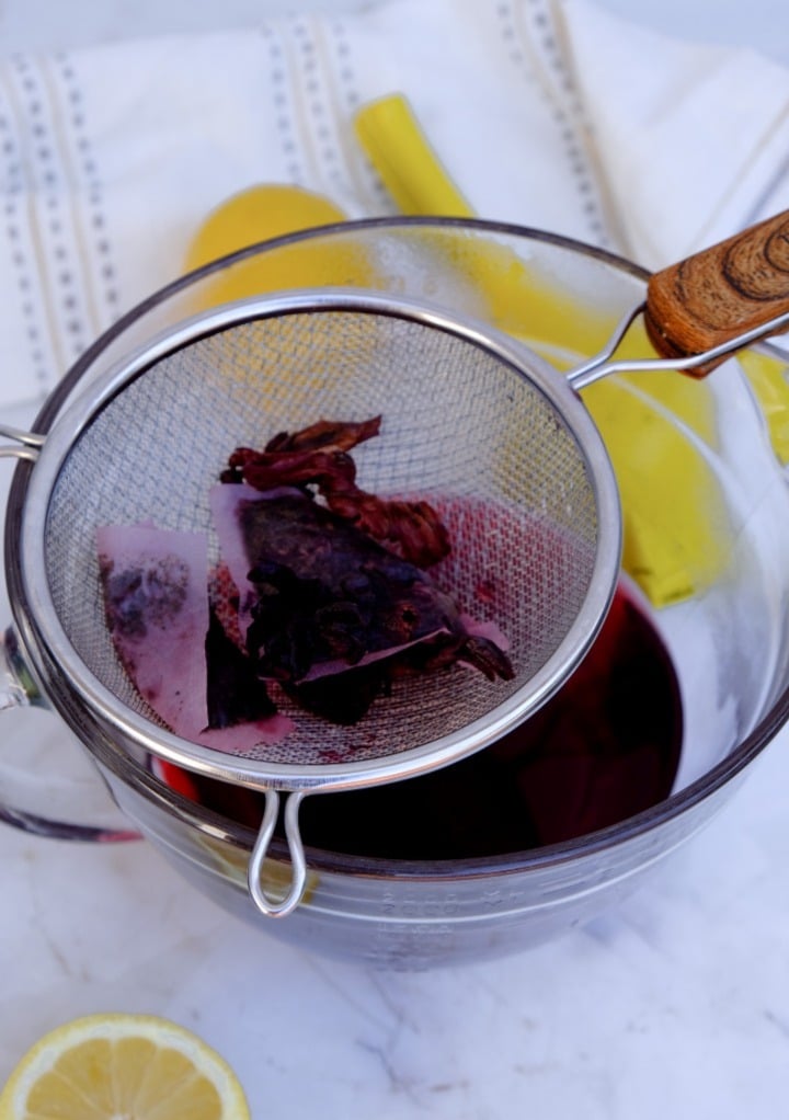 Straining hibiscus flowers and tea bags over a glass  bowl.