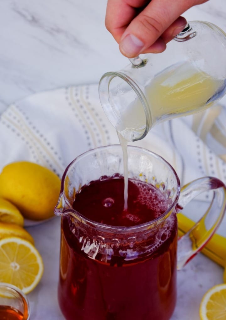 Fresh lemon juice being poured into hibiscus tea.