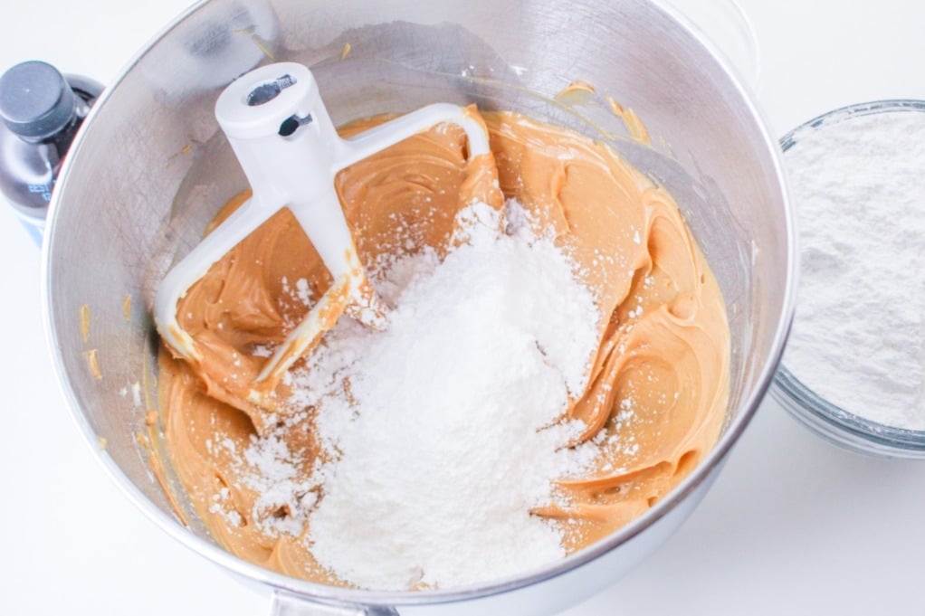 Powdered sugar added to peanut butter mix to make frosting in a mixing bowl. 