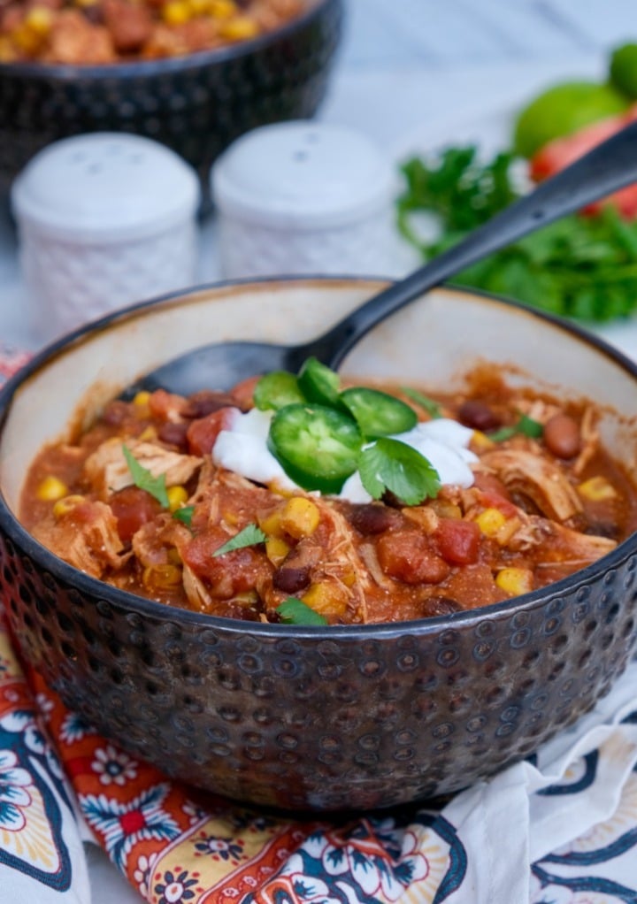 Chicken taco soup in a brown serving bowl topped with sour cream and sliced jalapenos. 