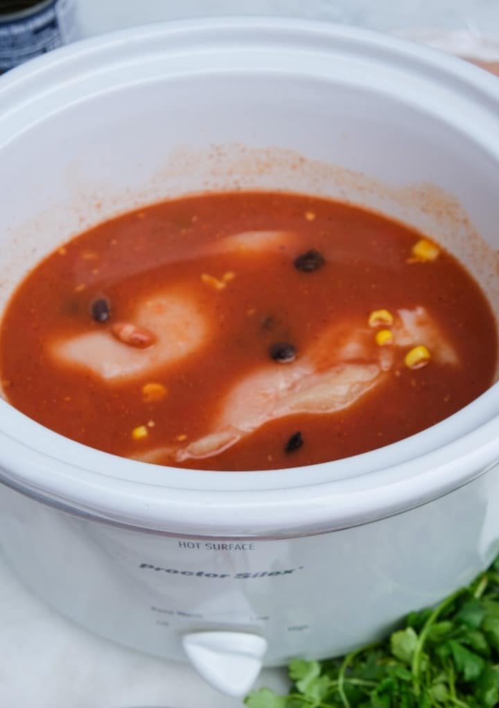 Uncooked chicken breasts added to the soup mixture before cooking in a slow cooker. 