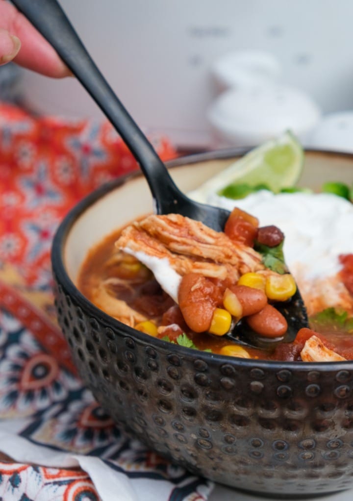 Spoonful of chicken taco soup from a brown serving bowl. 