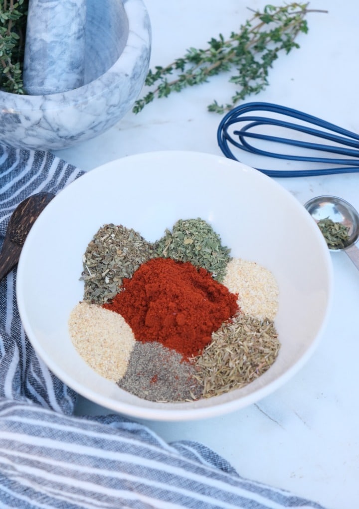 steak seasoning spices in a small white bowl with a blue whisk on the side. 