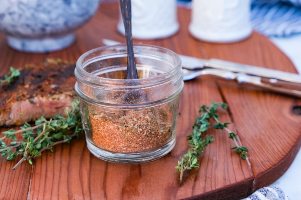 Steak seasoning mix in a small clear mason jar with fresh herbs on the side. 
