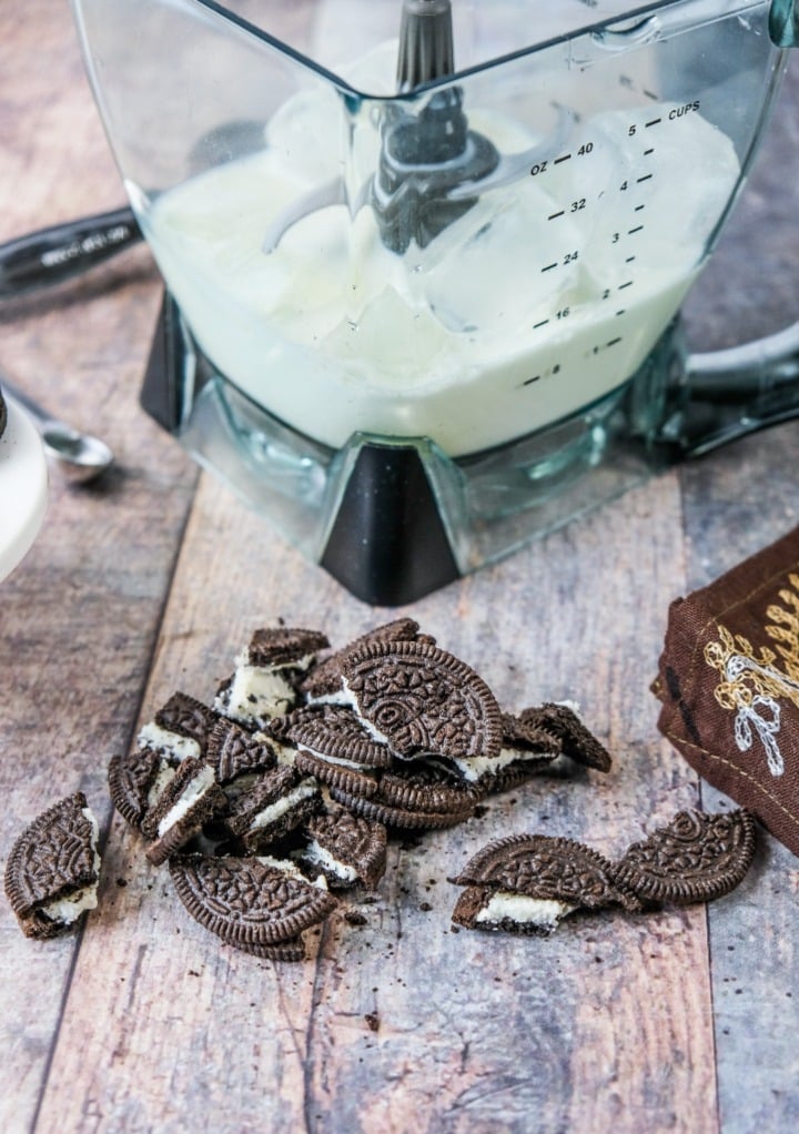 Crushed Oreo cookies with a blender in the background with milk and ice. 