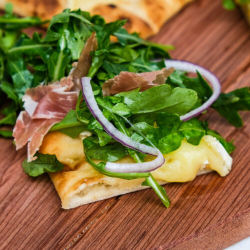 A slice of arugula pizza with sliced onion.