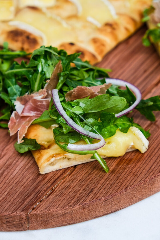 A slice of arugula pizza with sliced onion. 