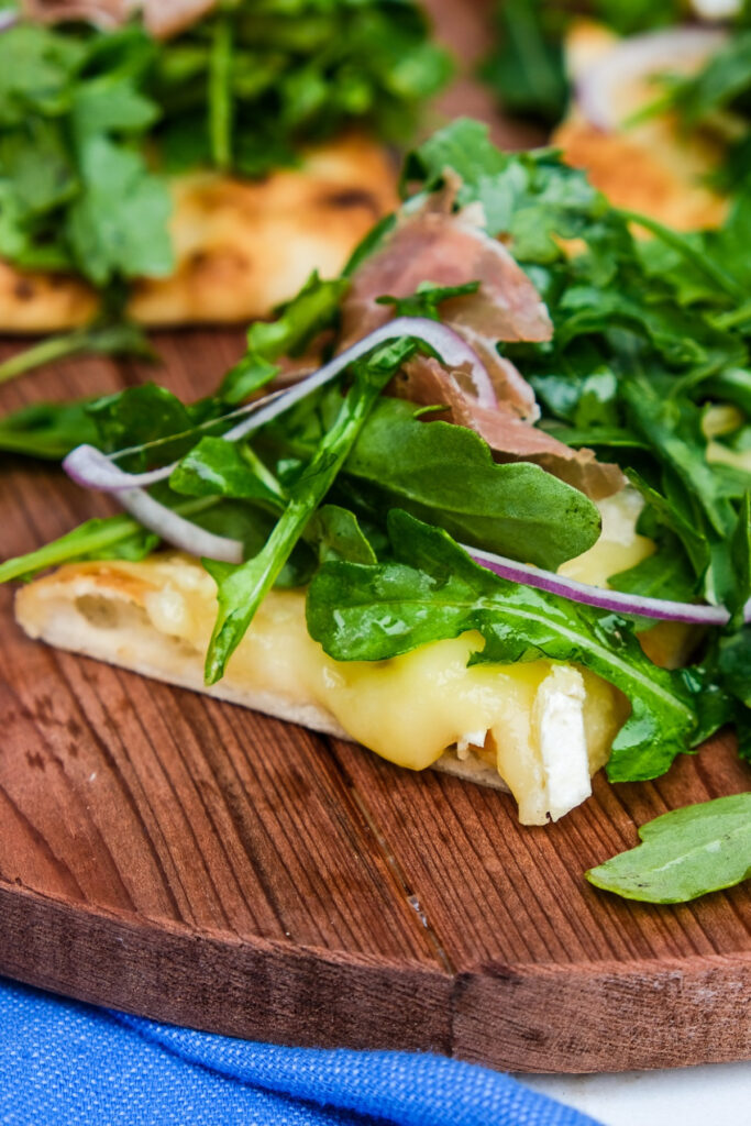 Arugula pizza with brie cheese and topped with prosciutto.