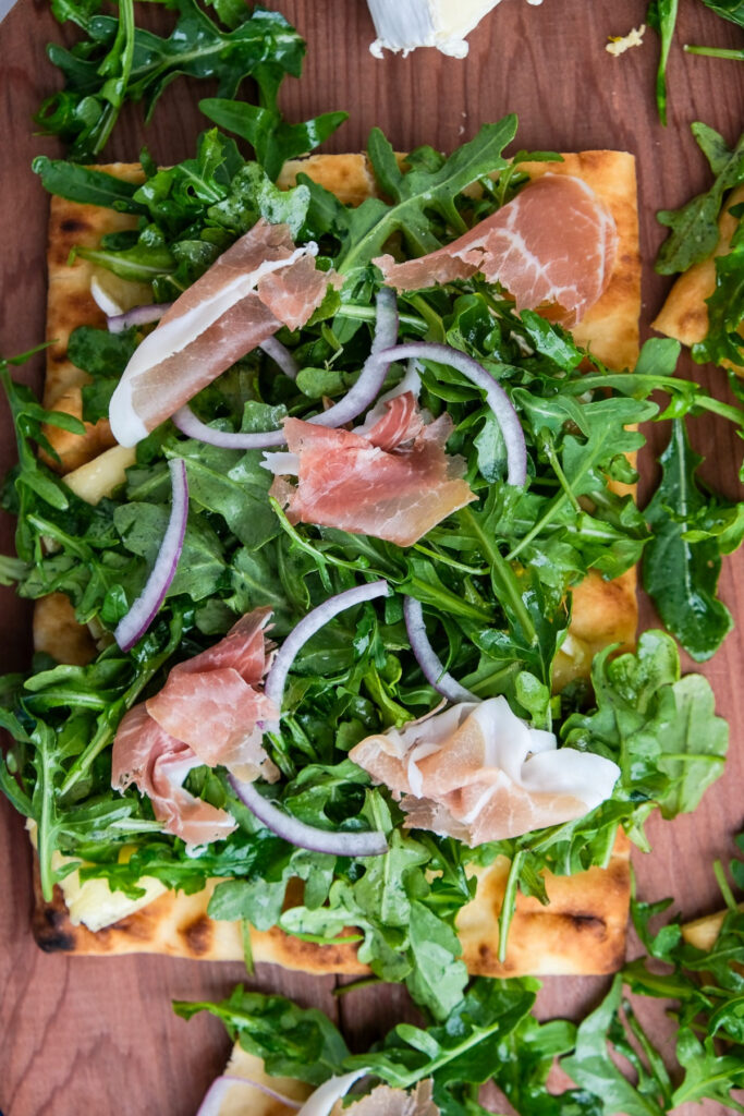 Top view of pizza topped with arugula, red onion and prosciutto.