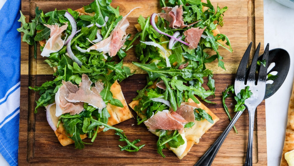 Arugula pizza topped with prosciutto and sliced onion. 