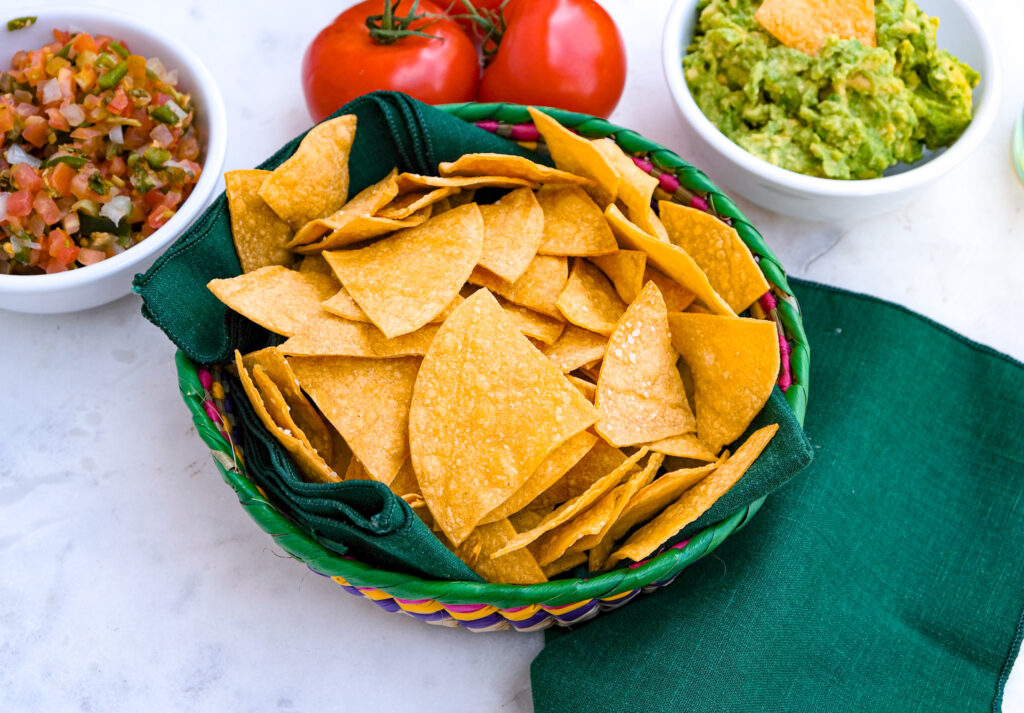 Healthy tortilla chips in a basket with salsa and guacamole on the side. 