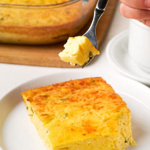 Slice of green chile egg casserole on a white dish with a fork taking a bite off.