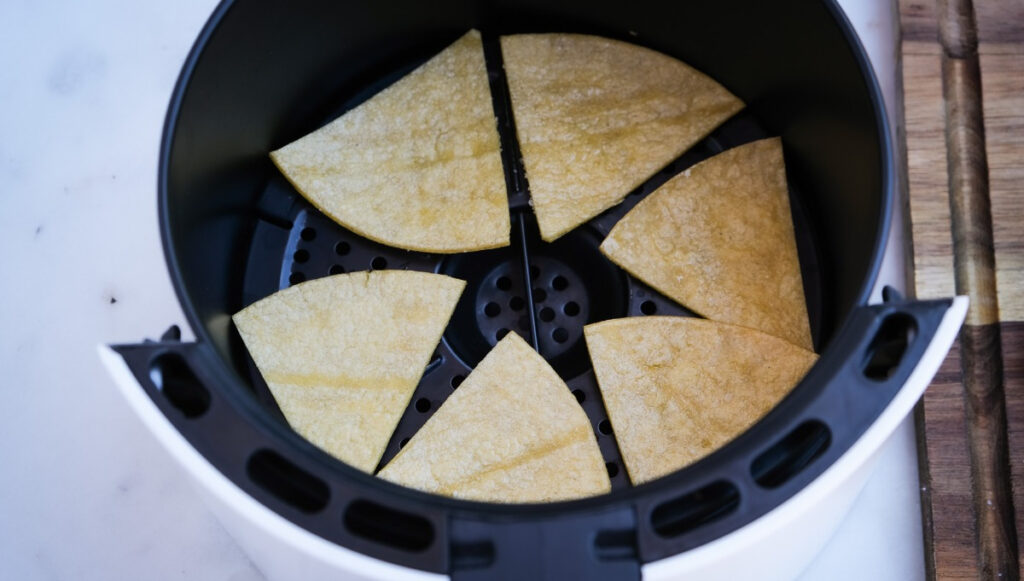 Triangle corn tortillas in the center of the air fryer before cooking.