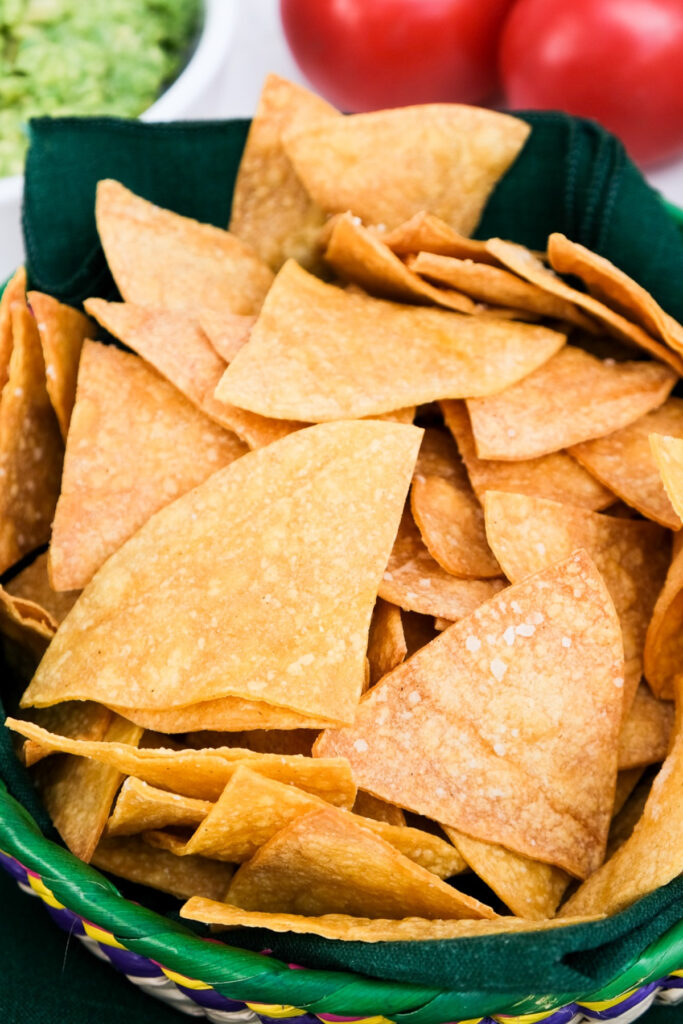 Healthy tortilla chips in a straw basket with a green rim. 