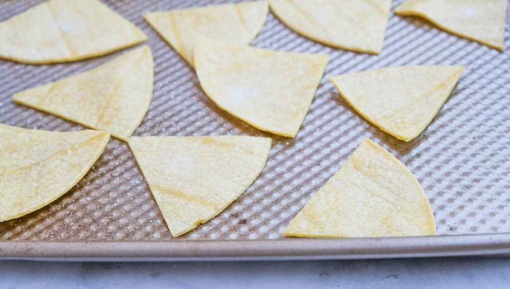 Sliced corn tortillas on a baking sheet ready to bake into chips. 