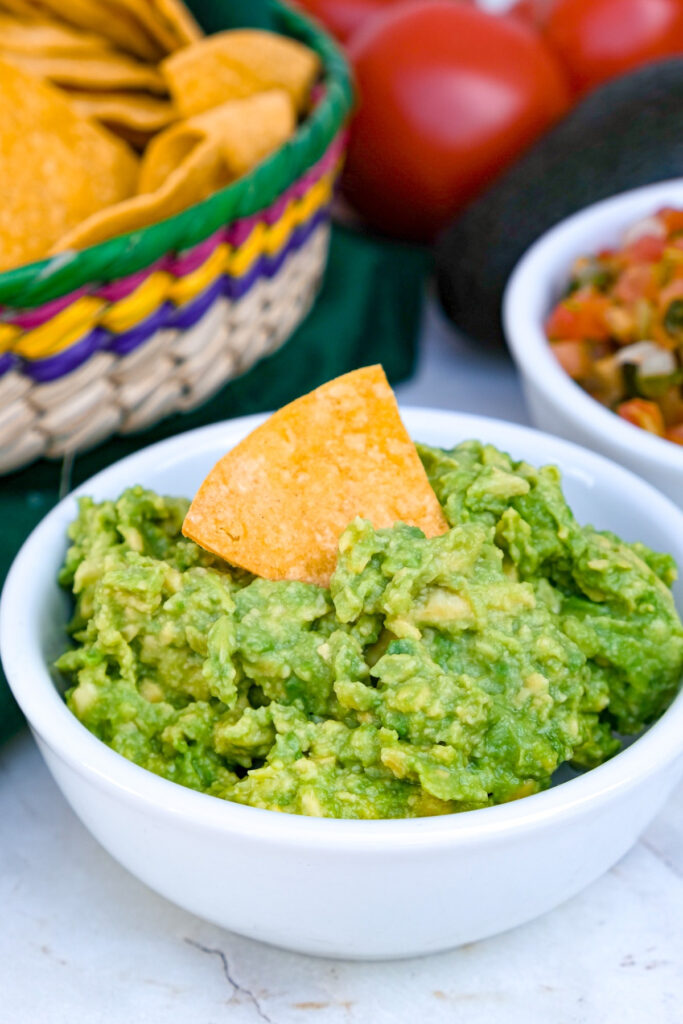 White bowl with guacamole with a tortilla chip in the middle. 