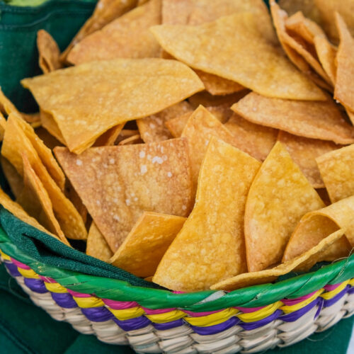 Homemade tortilla chips in a straw basket.