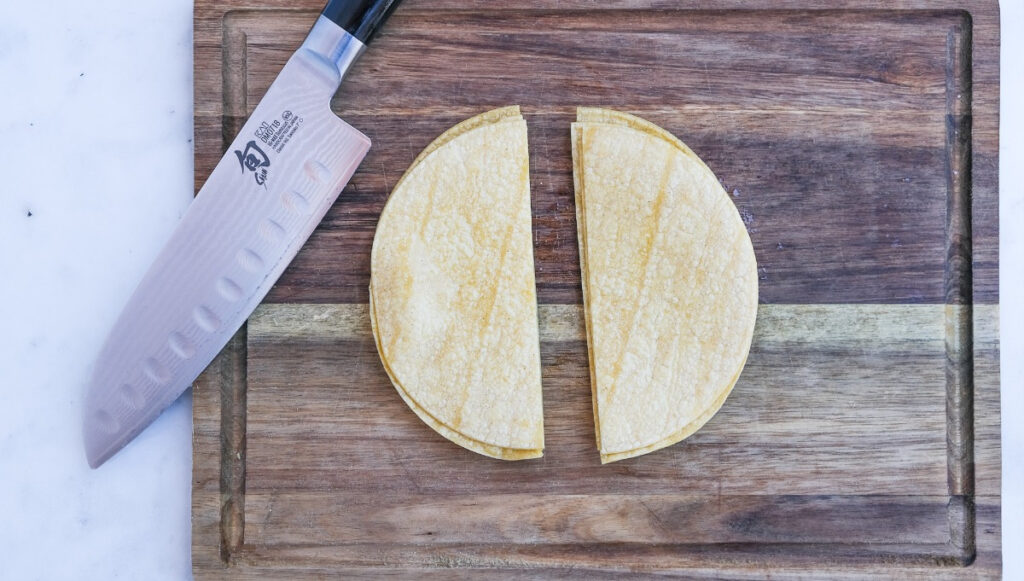 Corn tortillas on a brown cutting board cut in half. 