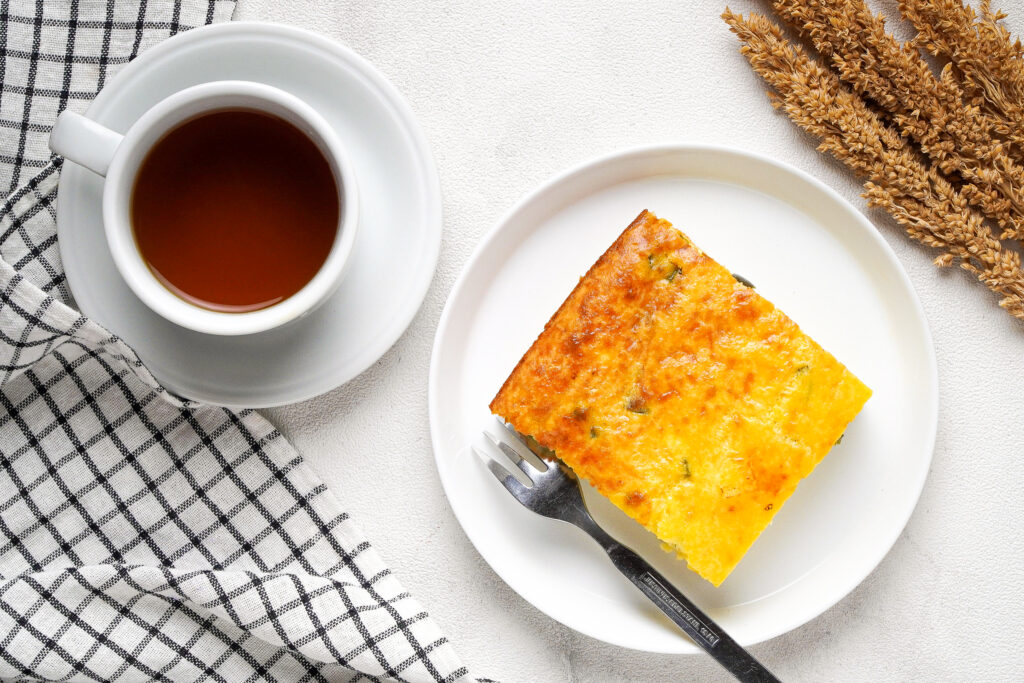 A slice of green chile egg casserole on a serving plate with coffee on the side.