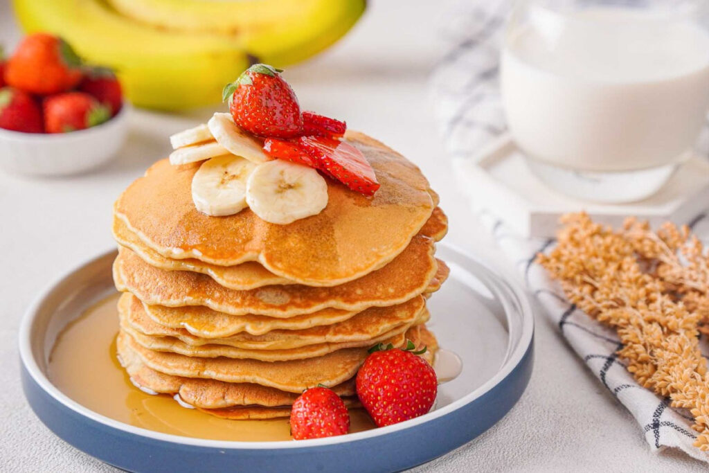 Banana oatmeal pancakes topped with maple syrup and sliced fruit. 