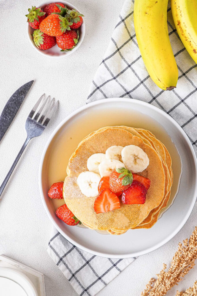 Top view of a stack of pancakes topped with sliced bananas and strawberries. 
