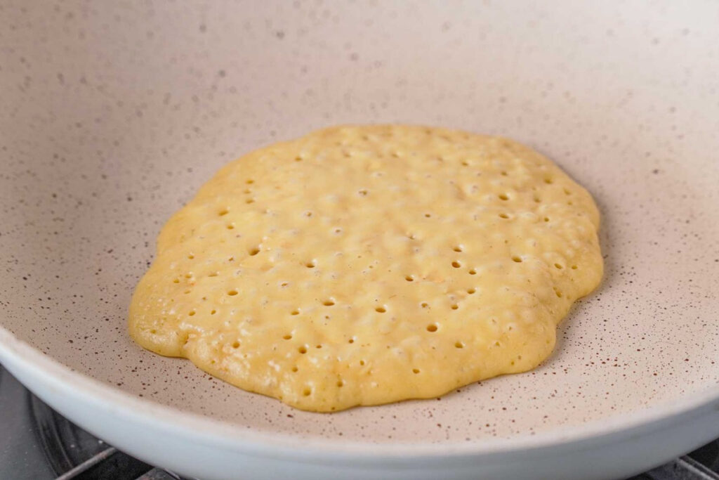 A pancake on a skillet cooking before turning it over to cook the other side. 