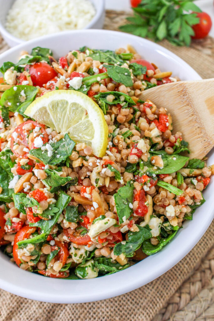 White serving bowl with Israeli couscous salad with a slice of lemon in the center. 