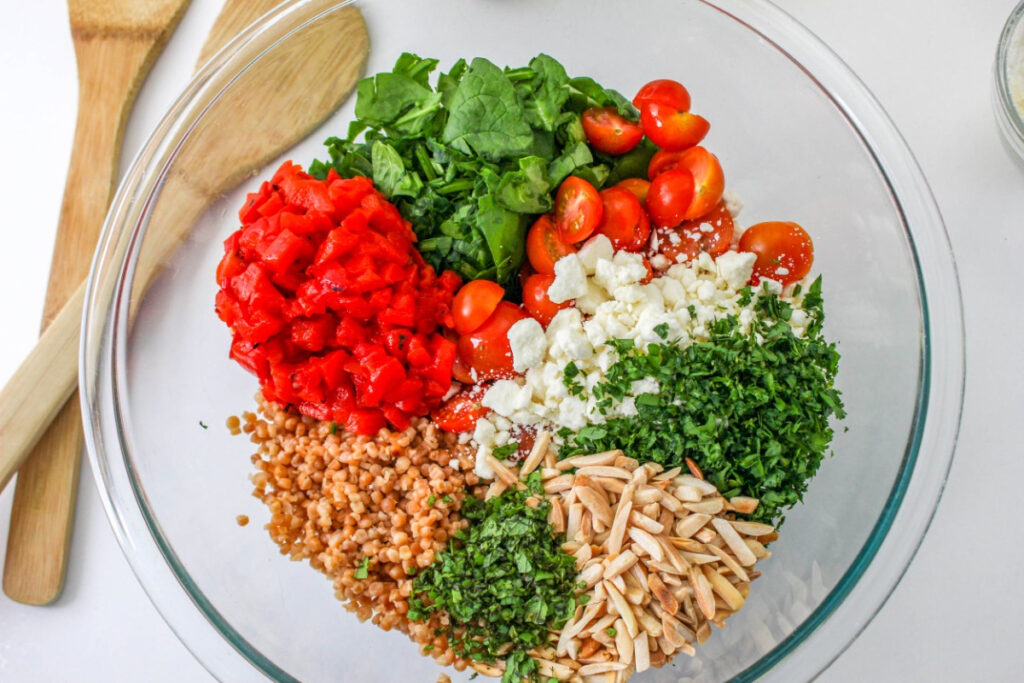 A large clear mixing bowl with ingredients for Israeli couscous recipe.