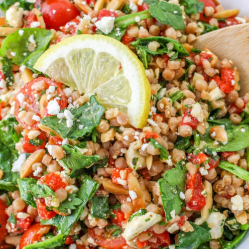 Israeli couscous salad recipe in a white serving bowl with a wooden spoon ready to serve.