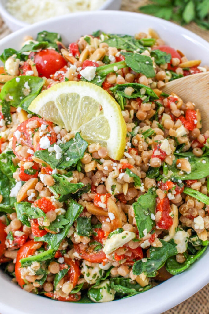 Israeli couscous salad recipe in a white serving bowl with a wooden spoon ready to serve.