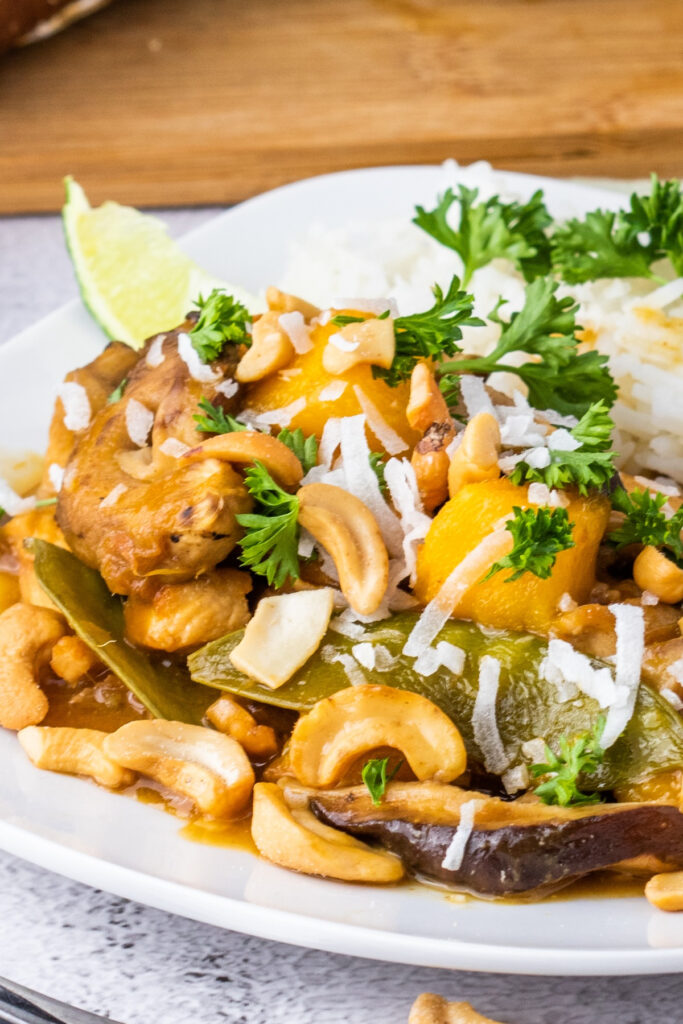 Asian inspired chicken stir fry with mangos and coconut on a white dinner plate. 