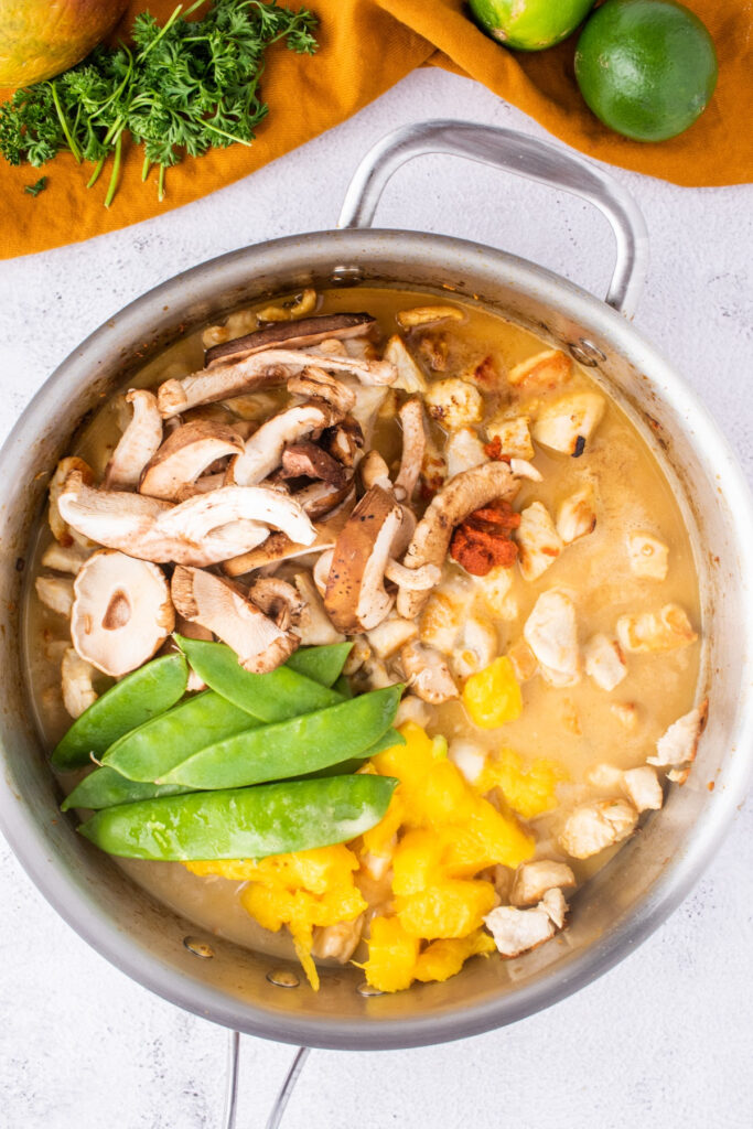 Large skillet with sauce and vegetables folded into cooked chicken. 