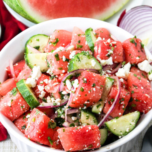 Watermelon salad with mind in a white serving bowl with a quarter of fresh watermelon on the side.