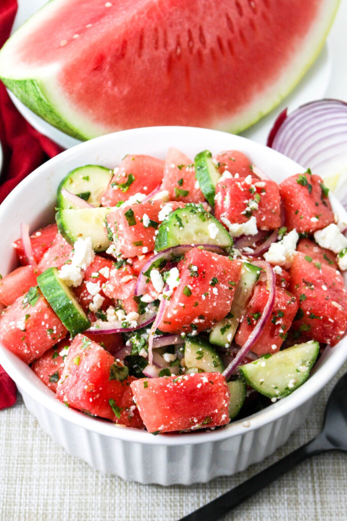 Watermelon salad with mind in a white serving bowl with a quarter of fresh watermelon on the side. 