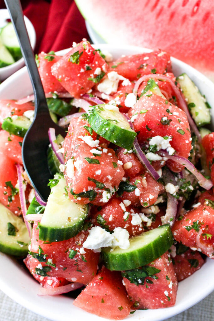 Spoonful of summer salad made with diced watermelon in a white serving bowl. 