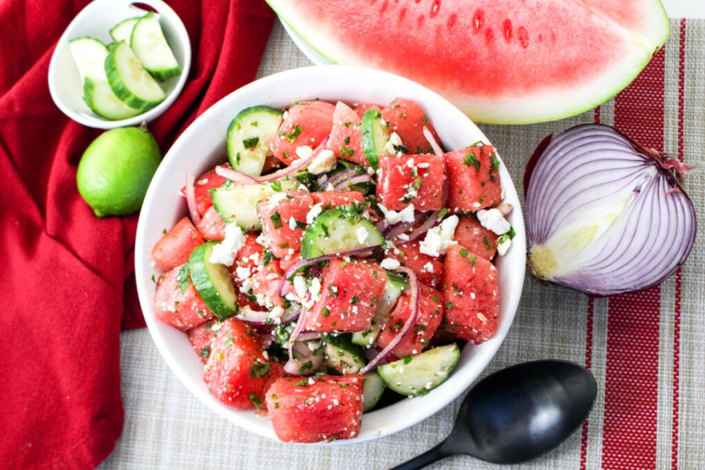 Summer salad in a white serving bowl with garlic and a lime on the side of the serving bowl. 