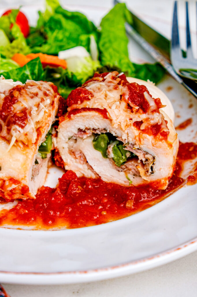 Sliced chicken stuffed with broccolini, cheese and prosciutto on a white dinner plate.