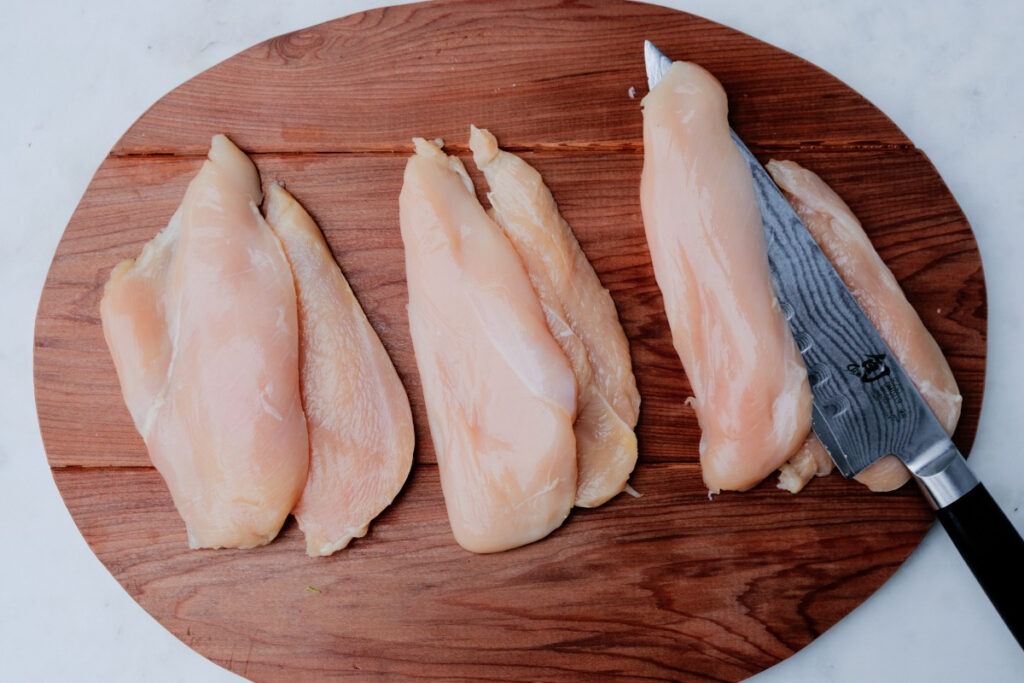 Chicken breasts on a cutting board sliced in half. 