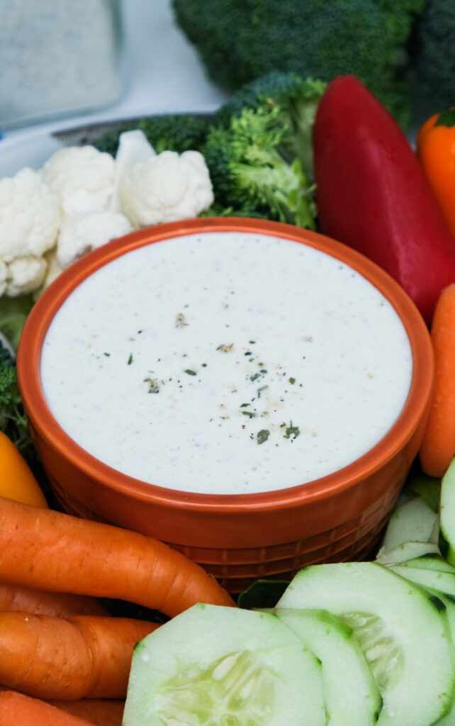 Ranch dip in an orange bowl with vegetables around the bowl.