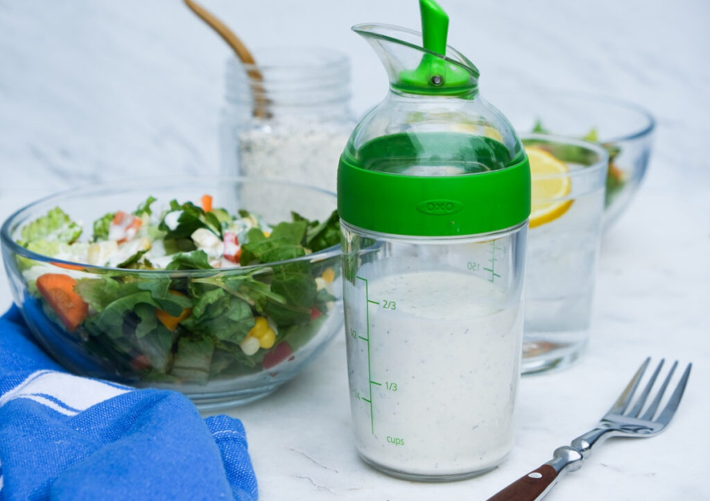 Salad dressing in a salad jar with a bowl of salad in the background.