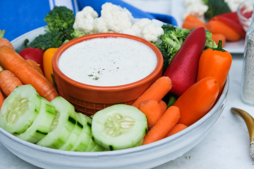 Large bowl of vegetables surrounded with a ranch dipping dressing. 