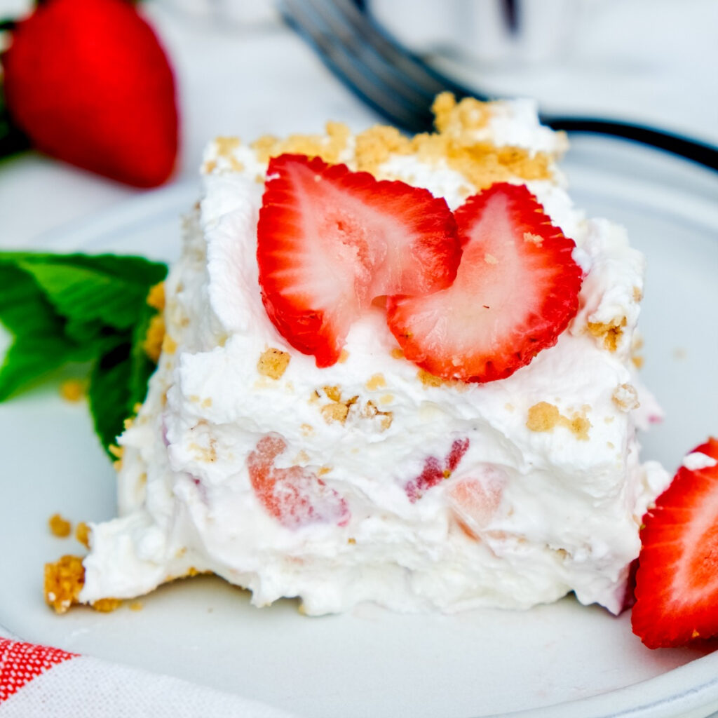 A slice of strawberry cream cheese icebox cake on a white dish with fresh sliced strawberries.