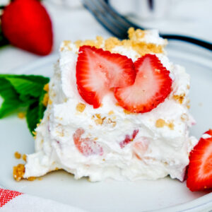 A slice of strawberry cream cheese icebox cake on a white dish with fresh sliced strawberries.