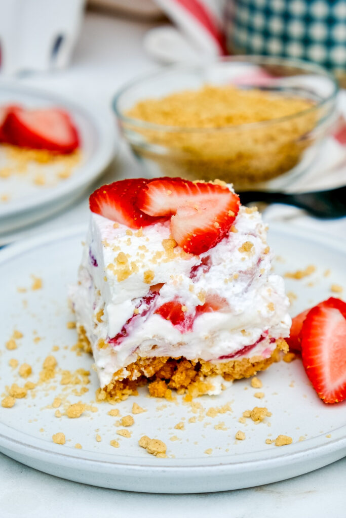 A slice of no-bake cake with whipped cream and sliced strawberries topped with cookie crumbs. 