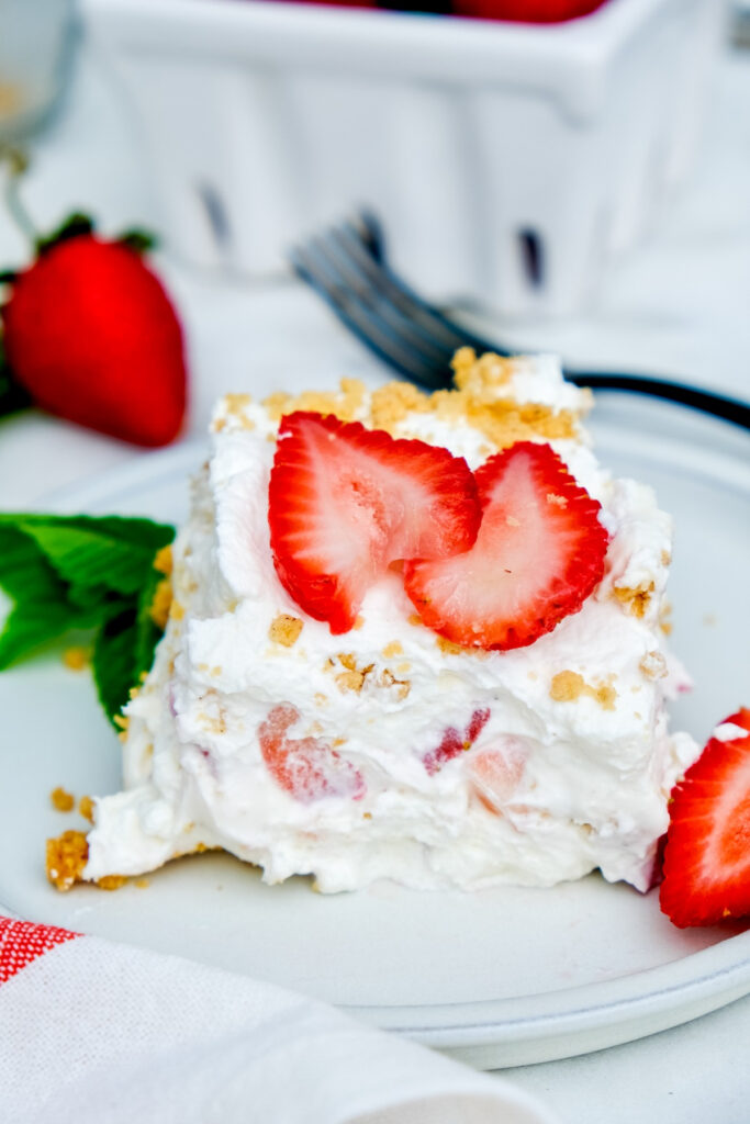 a slice of strawberry cream cheese icebox cake on a white plate topped with fresh strawberries. 