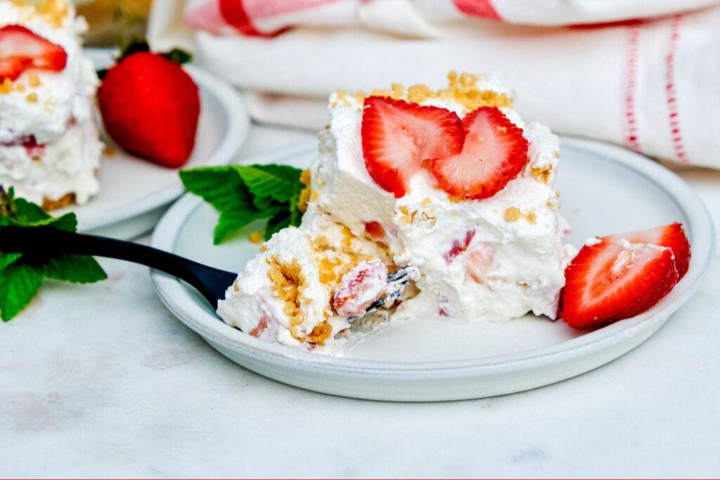 A slice of keto strawberry cream cheese icebox cake on a white plate with a fork scooping up a bite.