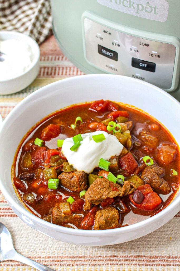 Sour cream on brisket chili served in a white bowl.