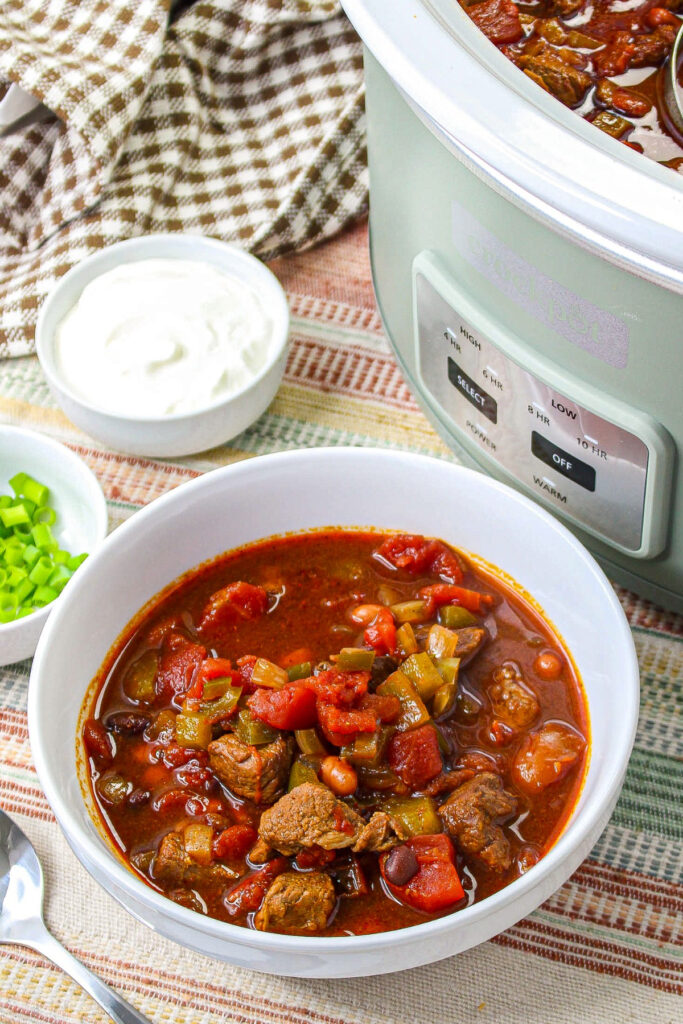 Chili in a white serving bowl with a crock pot on the side.