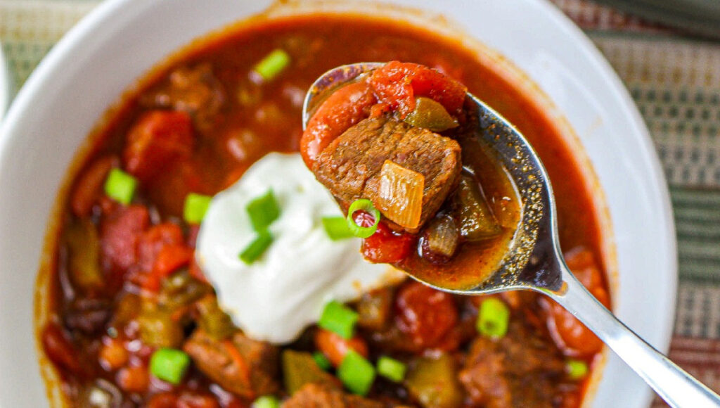 A white bowl of chili topped with sour cream and diced onion.